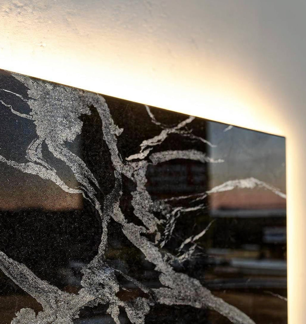 Luxury close-up of polished Black Python granite stone showing dramatic silver-grey veining, glossy reflections, and warm concealed backlighting behind the edge.