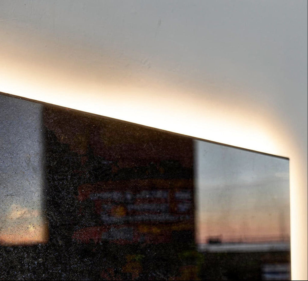 Close-up of polished Absolute Black Mirror stone with glossy reflections and warm halo backlight glowing behind the slab edge.