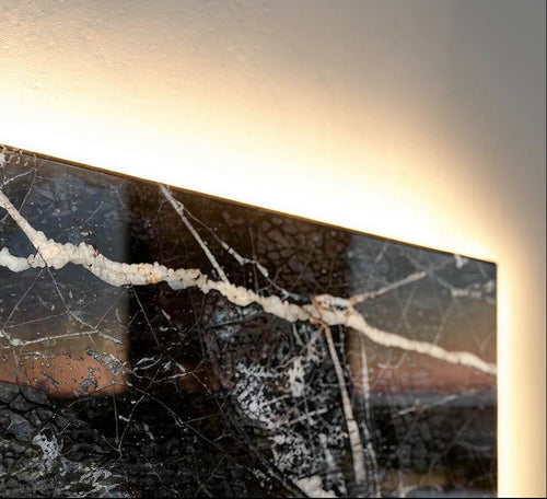  Luxury close-up of polished Noir Grand Antique marble showing dramatic white veining, glossy reflections, and warm concealed backlighting behind the slab.
