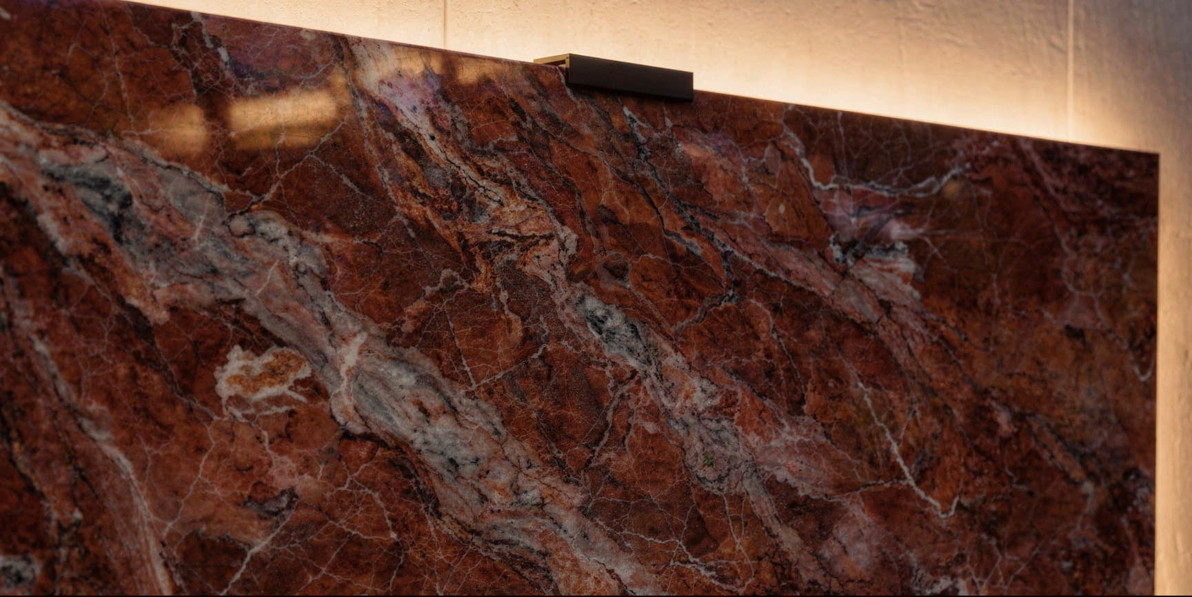 Luxury close-up of polished Rouge des Carpates marble showing warm red tones, natural veining, and concealed halo lighting behind the slab.